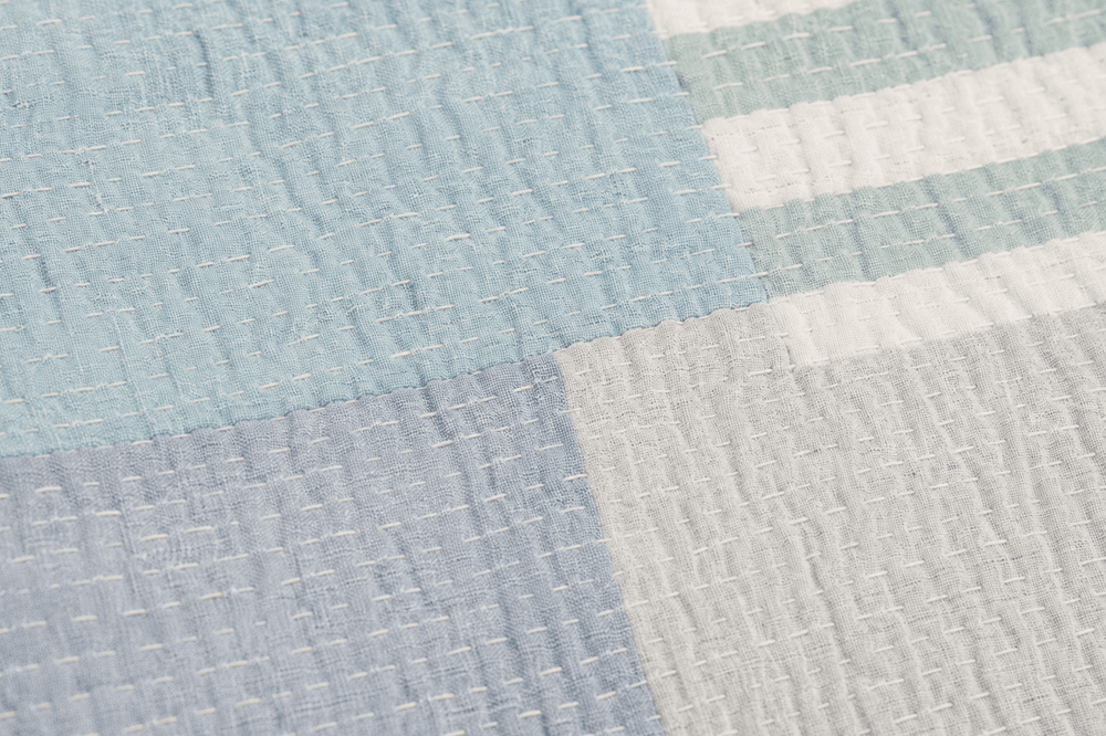 Detail of hand-stitched Kantha texture highlighting patchwork fabric blocks