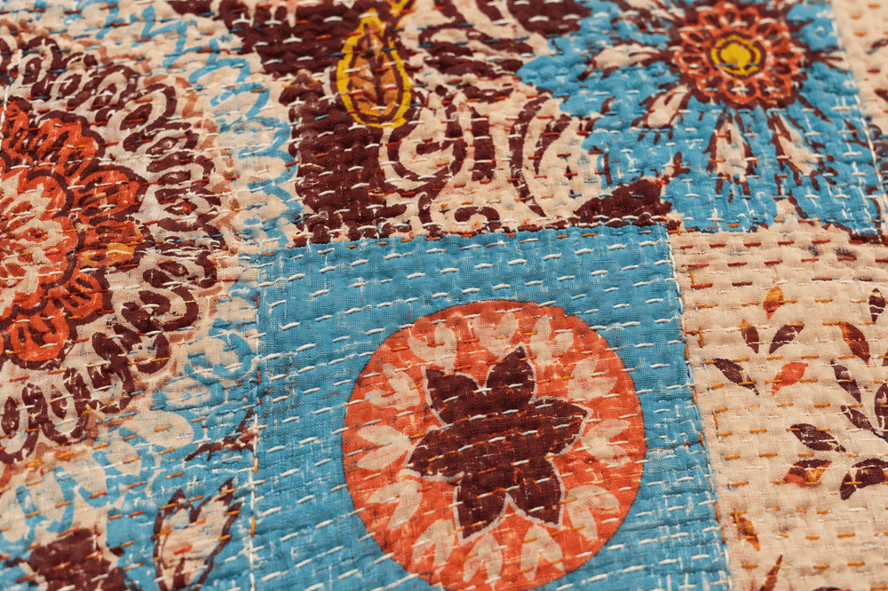 Detail of hand-stitched Kantha running stitch pattern highlighting patchwork fabric blocks