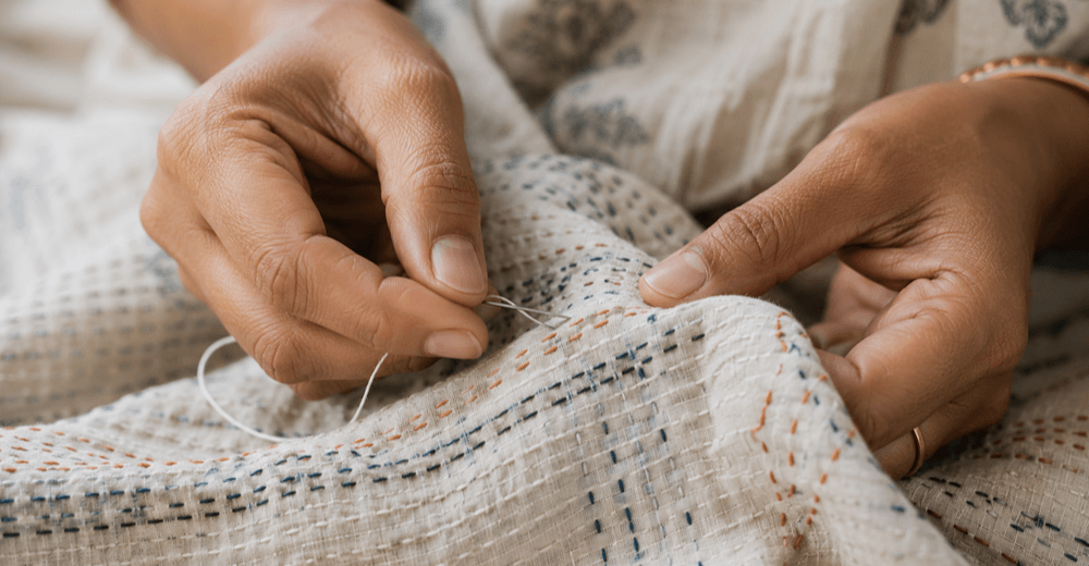 Artisan hand-stitching traditional Kantha running stitch on layered cotton fabric